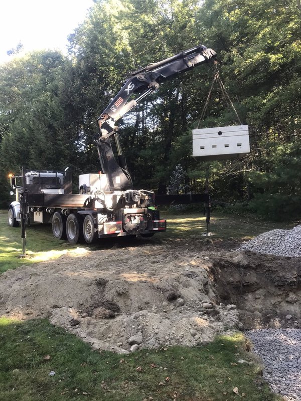 Crane lowering concrete drywell into excavation